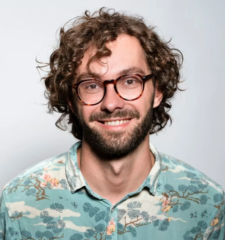 a man with curly hair and glasses smiling